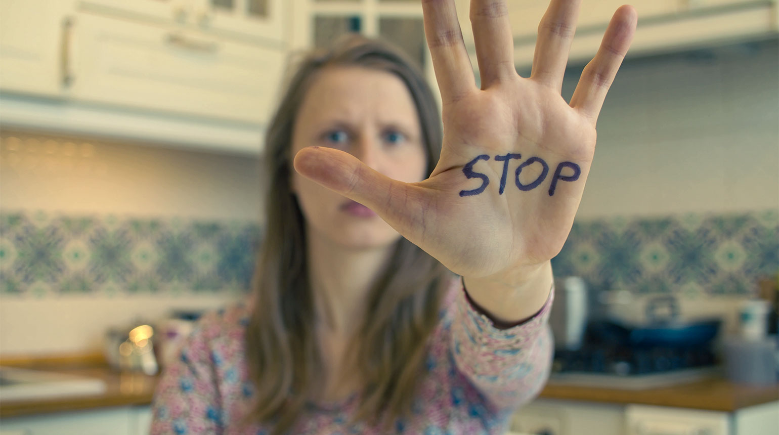 Symbolbild: Eine Frau streckt abwehrend ihre Hand aus; auf der Handfläche steht „Stop“.