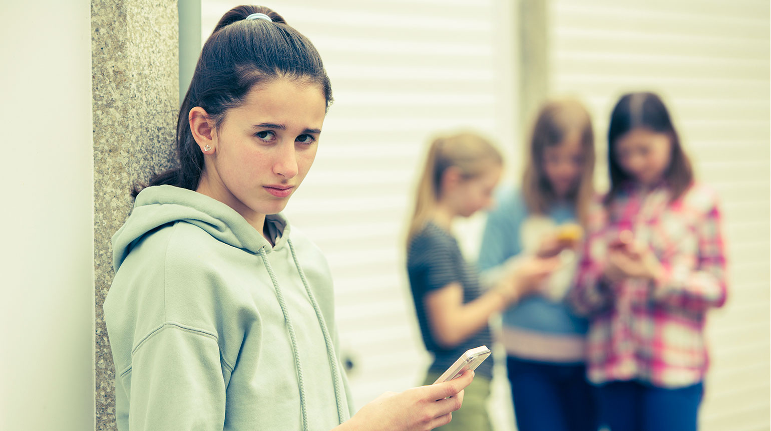 Eine Jugendliche hält ein Smartphone; sie sieht traurig und ängstlich aus.