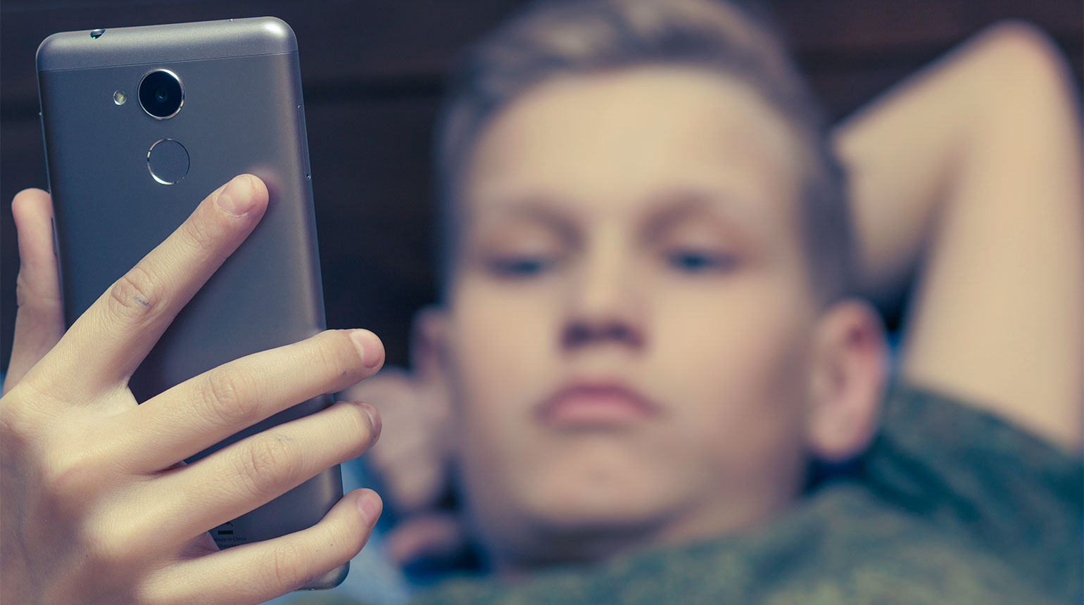 Ein Junge guckt ernst auf sein Smartphone. 