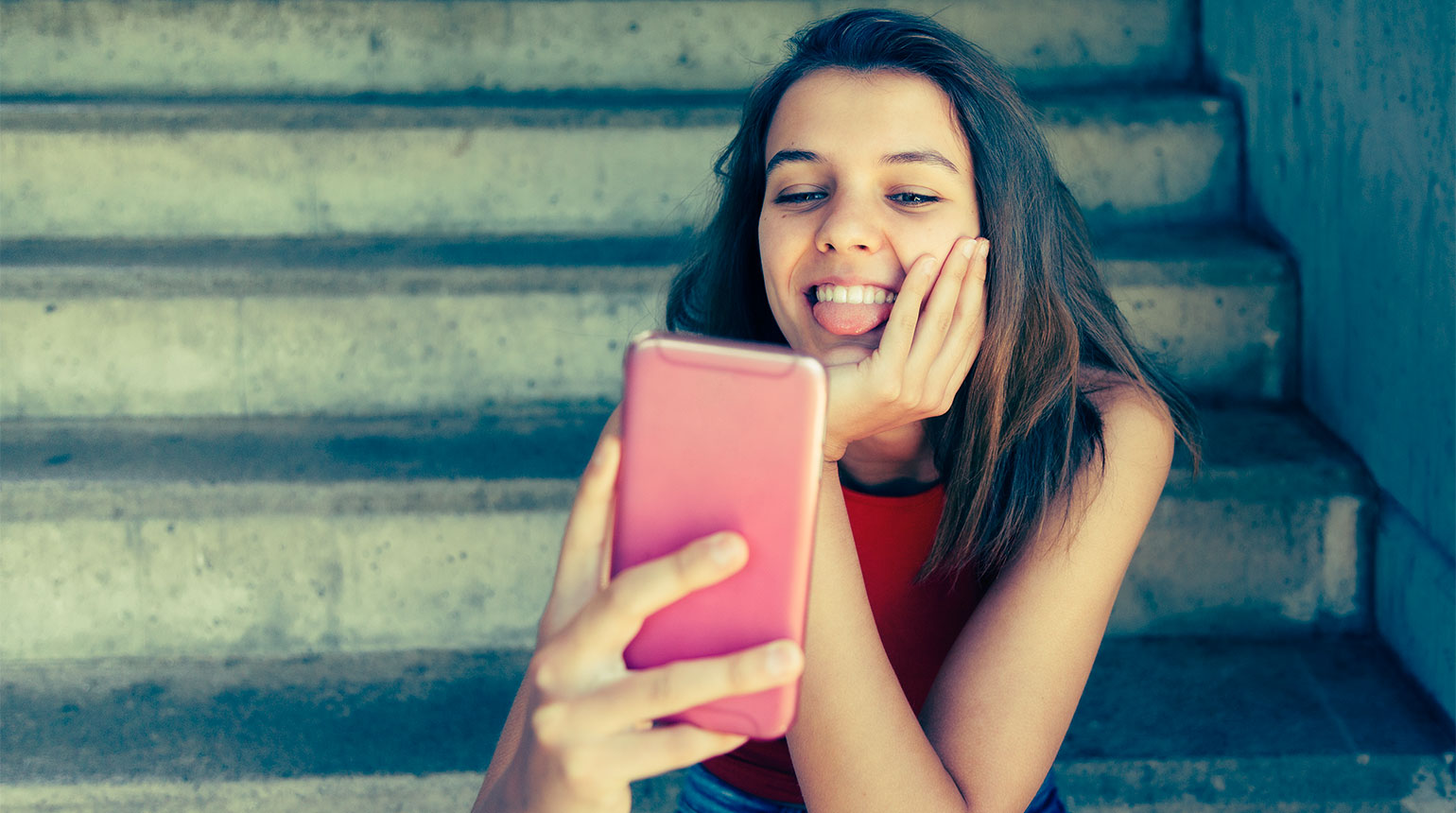 Symbolbild: Ein Mädchen schaut lächelnd auf sein Smartphone-Display. 
