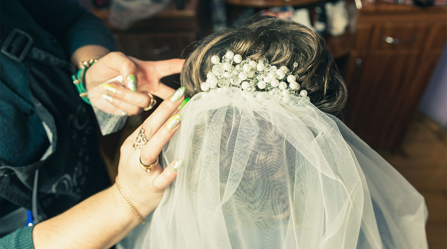 Nahaufnahme: Eine Frau steckt die Frisur einer verschleierten Braut fest.