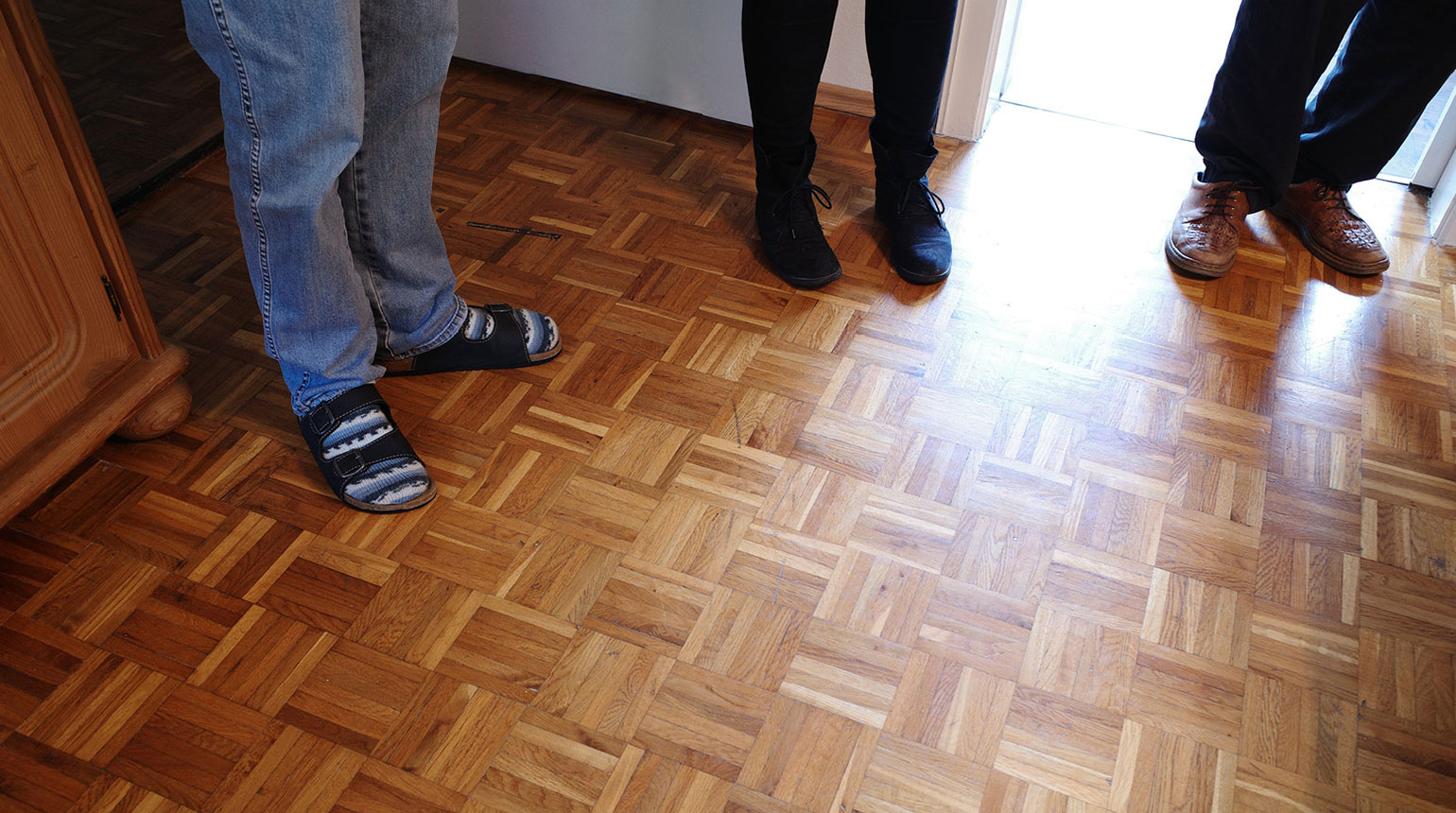 Detailaufnahme: die Füße von drei Menschen, die in einem Raum mit Holzboden im Halbrund stehen.  