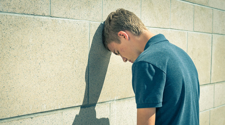 Ein Jugendlicher lehnt sich mit dem Kopf gegen eine Wand. Er wirkt verzweifelt. 