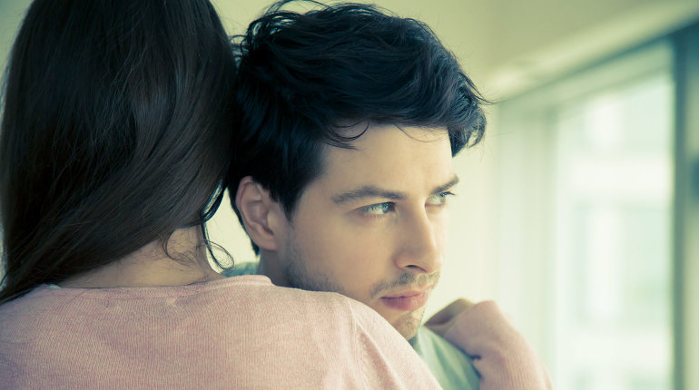 Eine junge Frau nimmt ihren Mann oder Partner tröstend in den Arm.
