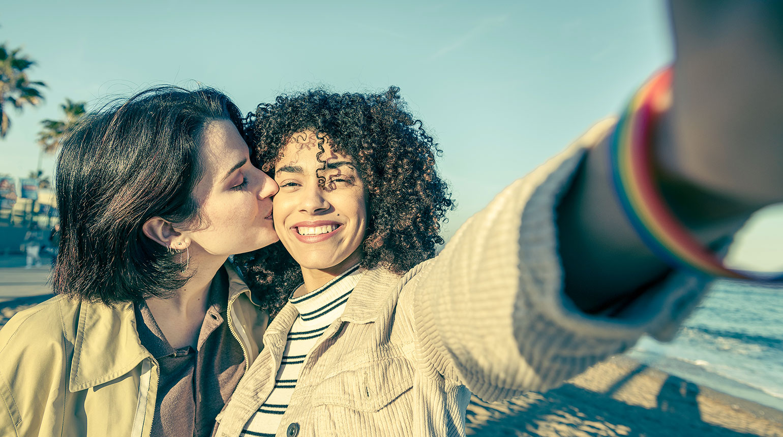 Zwei junge Frauen machen ein Selfie. Eine küsst die andere auf die Wange.