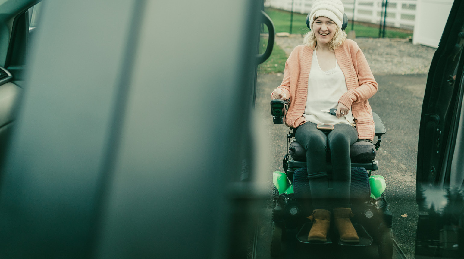 Eine junge Frau, modisch gekleidet, steht mit ihrem E-Rollstuhl bereit, um in ein Auto zu steigen.