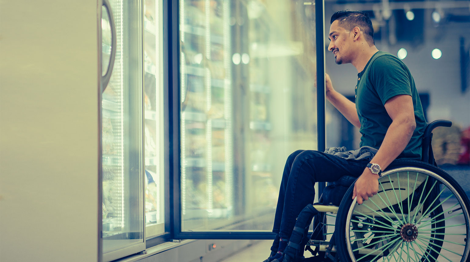 Ein junger Mann im Rollstuhl beim Einkaufen im Supermarkt.