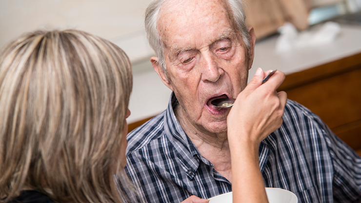 Eine Pflegekraft füttert einen älteren Mann.