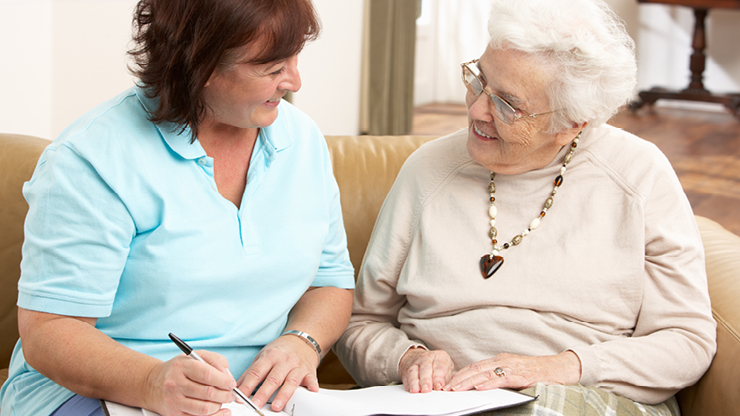 Eine Pflegekraft im Gespräch mit einer älteren Dame. Die Pflegekraft notiert mit.