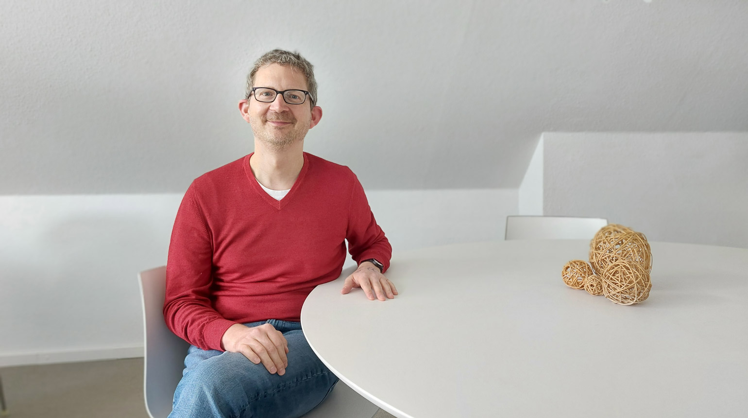 Foto: Dr. Tobias Skuban-Eiseler sitzt in Jeans und Pulli an einem Besprechungstisch. Er lächelt freundlich.
